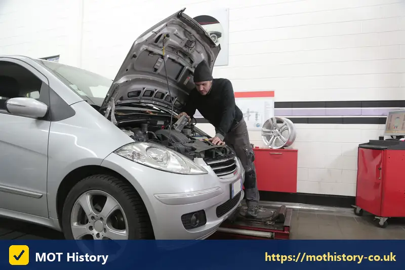 Mechanic working under the bonnet of a silver car - car garage