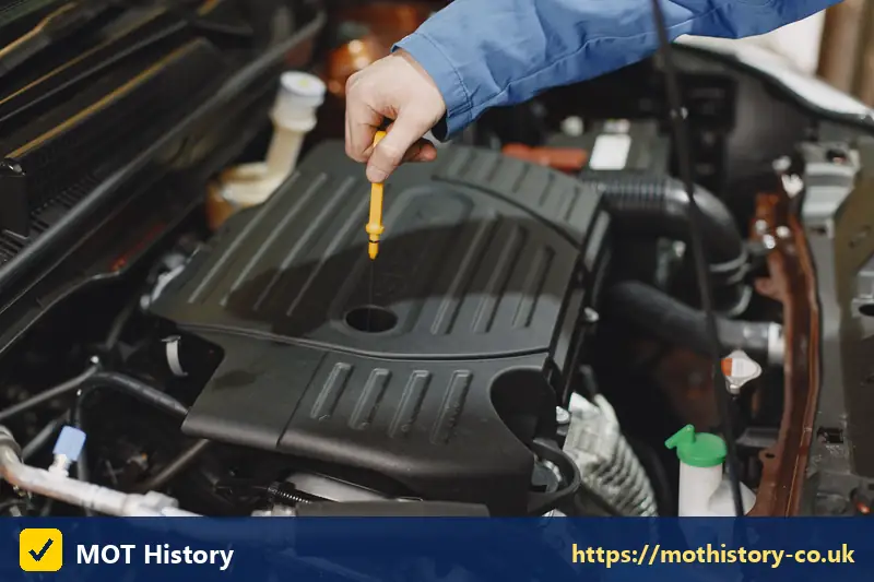 Hand checking engine oil with a yellow dipstick - car service station