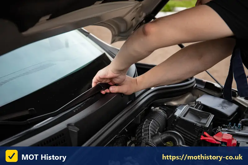 Hand reaching under a raised bonnet to check the engine bay - how long mot certificate valid for