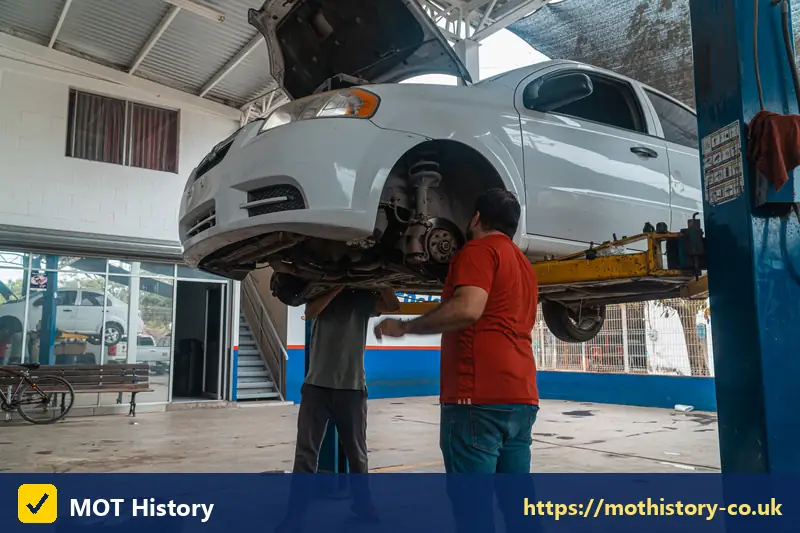 Two mechanics working beneath a car on a lift - insurance write off categories