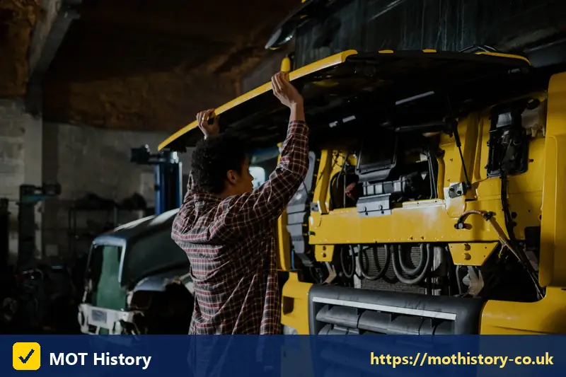 Mechanic checking under the cab of a yellow lorry - mot class checker by reg