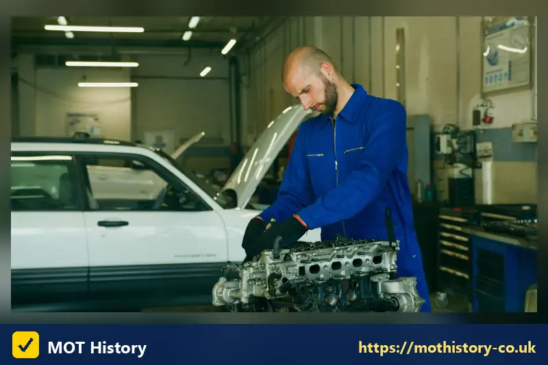 Mechanic holding an engine cylinder head beside a car - mot failure rules