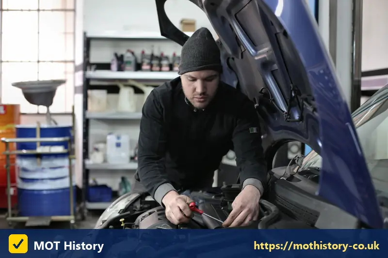 Mechanic working on a blue car engine in a garage - mot history
