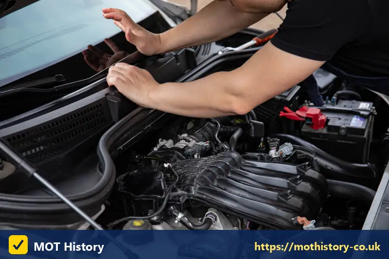 Mechanic leaning into the engine bay of a car - mot how far in advance