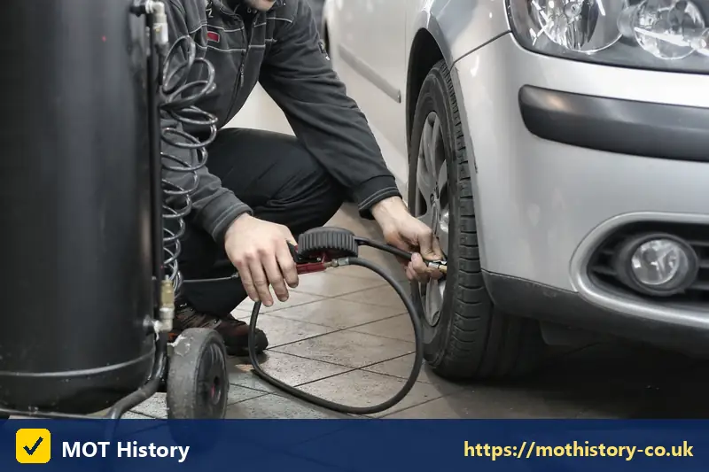 Mechanic inflating a car tyre in a garage - mot meaning car