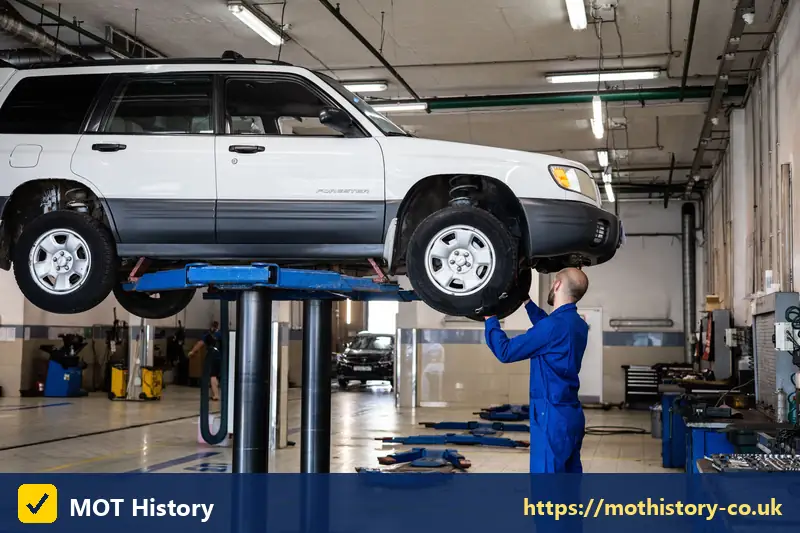 White car raised on a two-post lift in a garage - mot vehicle history check