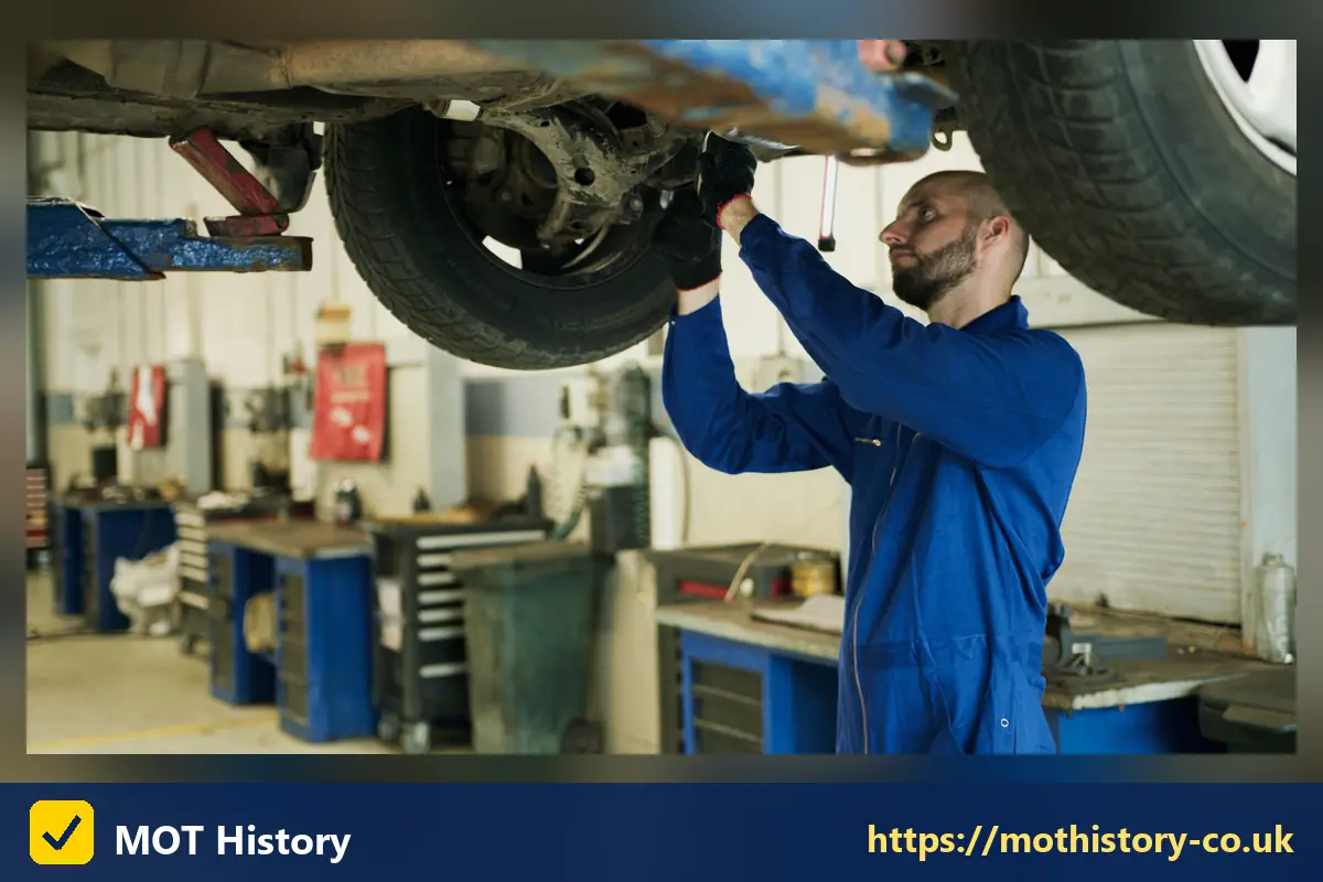 Mechanic inspecting the underside of a car on a lift - mot meaning