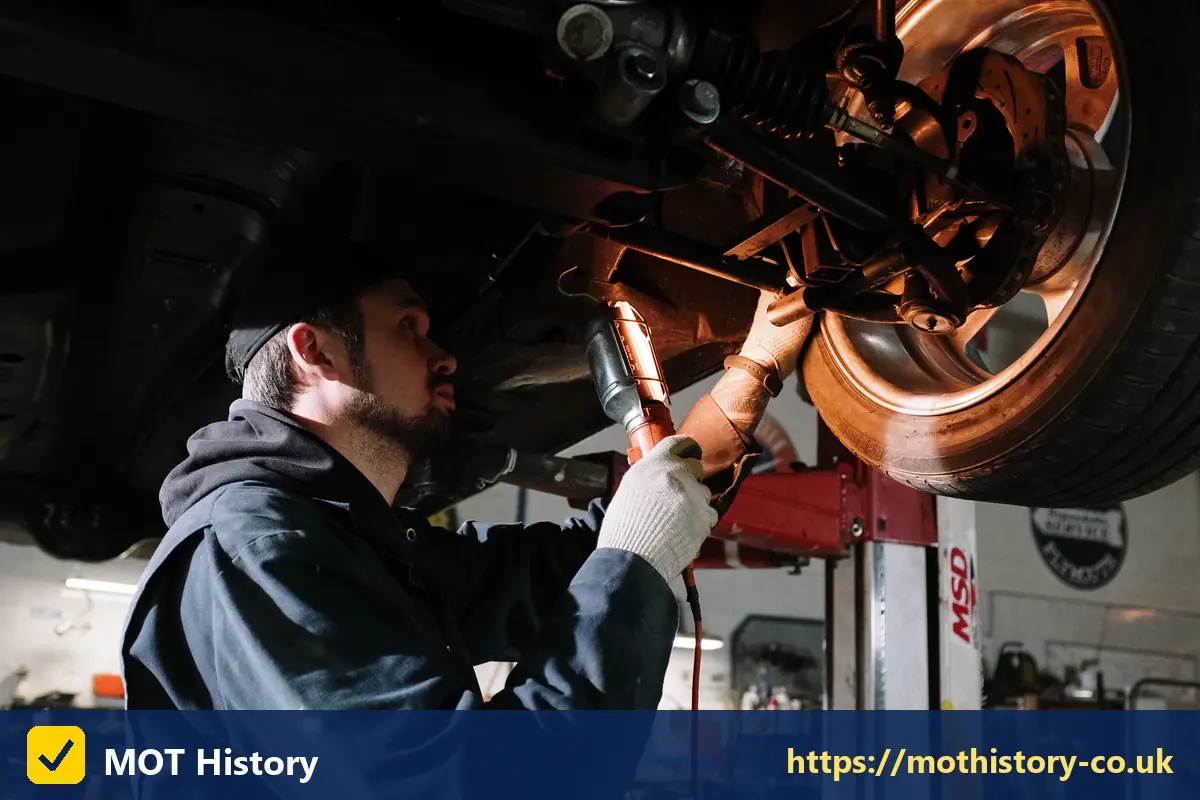 Mechanic inspecting brakes and suspension with a torch - mot retest ni